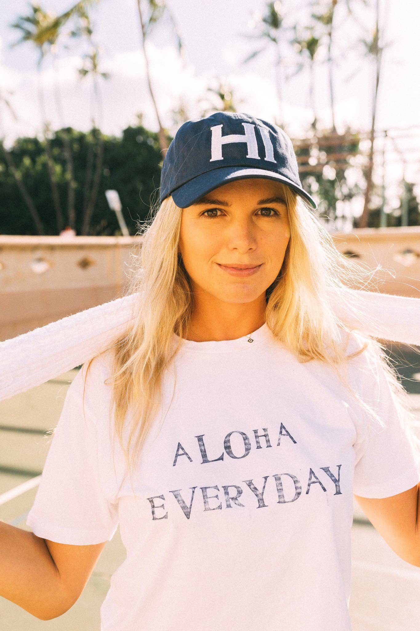 Woman wearing a cap and 'Aloha Everyday' t-shirt with palm trees in the background